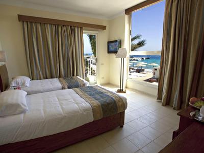 Chambre d'hôtel avec deux lits, vue sur la mer et la plage à travers de grandes fenêtres.