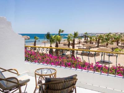 Blick von einer Terrasse mit Stühlen und Tisch auf Palmen, Meer und blauen Himmel im Hintergrund.
