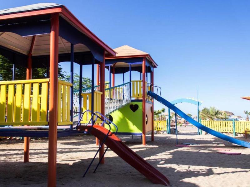 Bunter Kinderspielplatz mit Rutschen, Klettergerüst und Sandboden unter blauem Himmel.