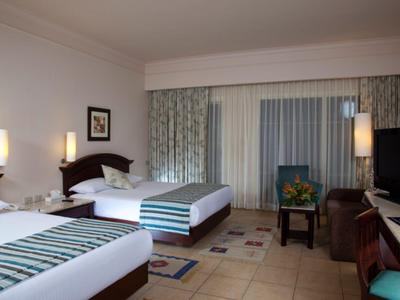 Pokój hotelowy z dwoma łóżkami, szafkami nocnymi, telewizorem i oknem z zasłonami.