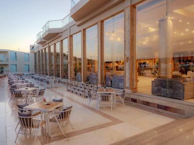 Hotel terrace with tables and chairs beside large glass windows at dusk.