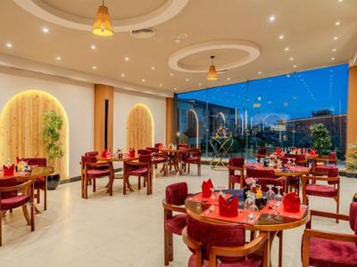 Modern hotel dining room with round tables, red chairs, and large windows at evening.