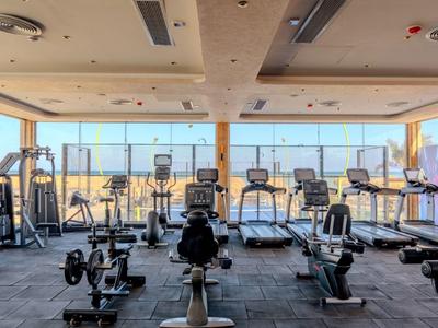 Modern gym with treadmills and strength machines, bright windows with a view.