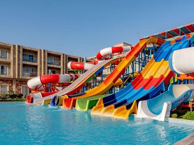 Colorful water slides lead into a large pool in front of a hotel building.