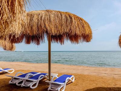 Beach with straw umbrellas and blue lounge chairs by the sea.