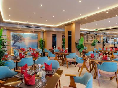 Modern hotel restaurant interior with blue chairs, wooden tables, and red napkins.