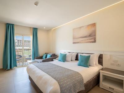 Modernes Hotelzimmer mit Doppelbett, türkisfarbenen Vorhängen und Balkon bei Tageslicht.