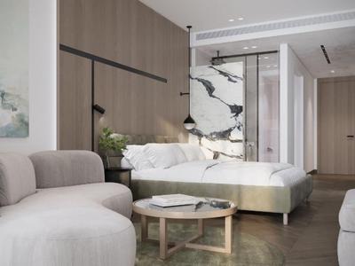 Modern ingerichte hotelkamer met beige fauteuil, tweepersoonsbed en marmeren wanddetail.