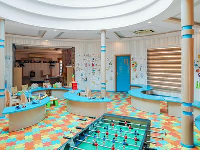 Sala giochi colorata con calcio balilla, tavoli, sedie e decorazioni murali.