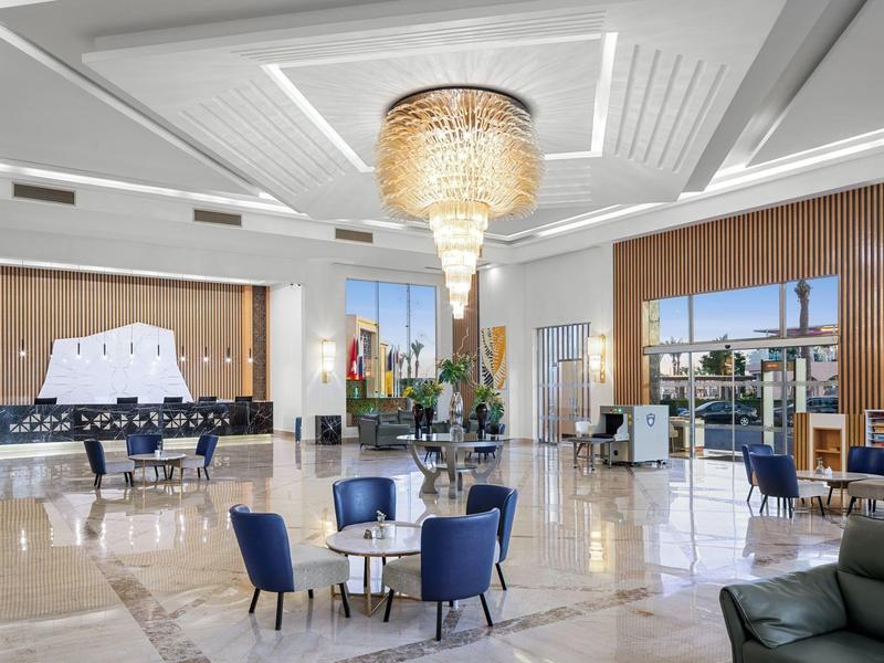 Ampia hall luminosa con sedie blu e grande lampadario in hotel moderno.