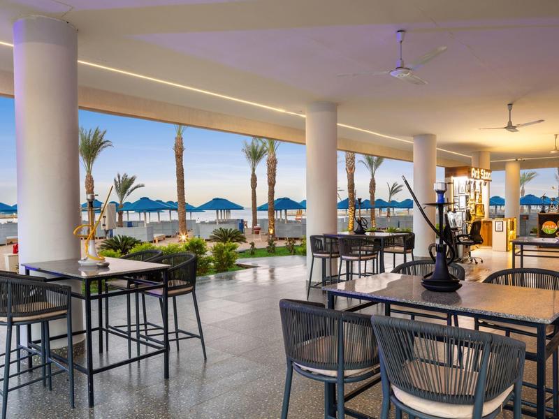 Terrazza del ristorante con vista sulla spiaggia e ombrelloni sotto un cielo sereno.
