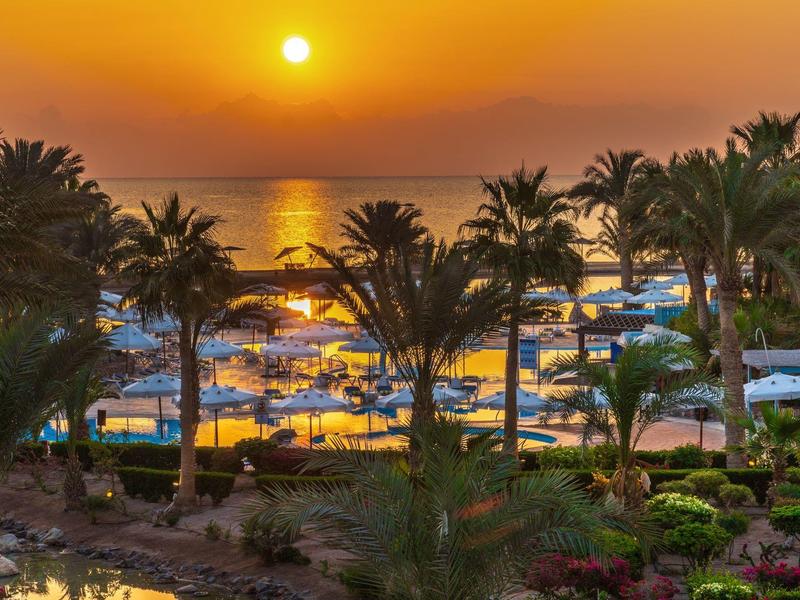 Tramonto su una spiaggia con palme e ombrelloni bianchi.