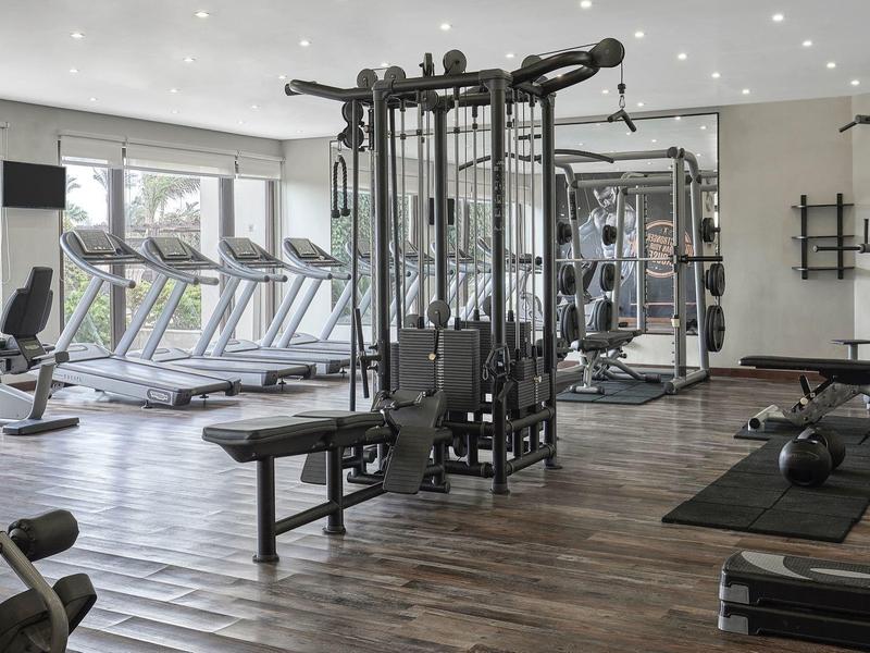 Moderne sportschool met apparatuur en loopbanden, lichte kamer met houten vloer en grote ramen.