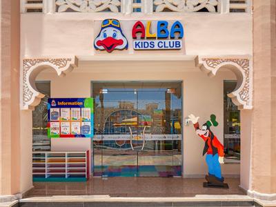 Eingang zum ALBA Kids Club mit einer Goofy-Figur neben der Glastür in einem hellen Gebäude.