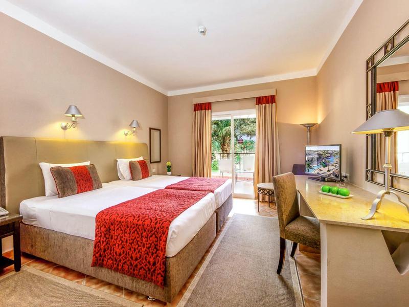 Jasny pokój hotelowy z łóżkiem podwójnym, czerwonym wystrojem i nowoczesnymi meblami.