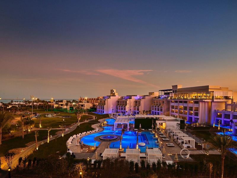 Vista de un hotel iluminado con zona de piscina al atardecer o anochecer.