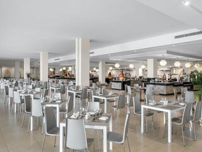 Ampia sala da pranzo moderna con tavoli bianchi e sedie grigie.