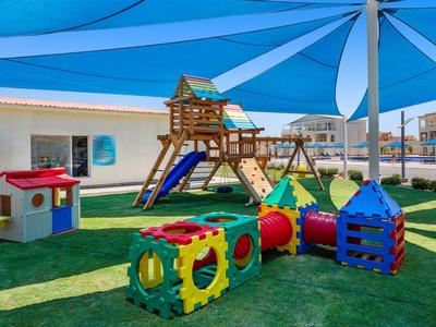 Parco giochi per bambini con struttura da arrampicata, scivolo, altalene e tunnel gioco sotto una tenda parasole blu.