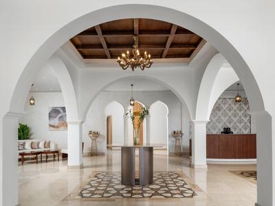 Ampia hall di hotel luminosa con archi, lampadario e decorazione centrale su tappeto