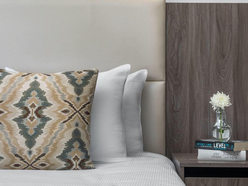 Letto accogliente con cuscino decorato e comodino con fiore e libri.