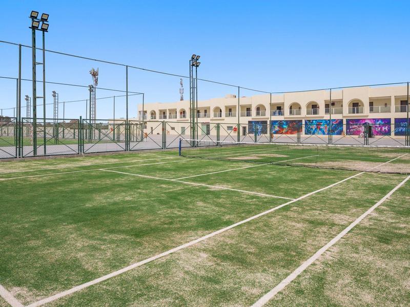Campo da tennis in erba sintetica vuoto davanti all'edificio dell'hotel in una giornata di sole.