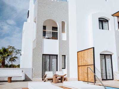 Modern white hotel with pool, lounge chairs, and wooden accents under a blue sky.