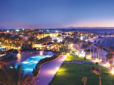Resort iluminado con piscina y jardín al atardecer junto al mar.
