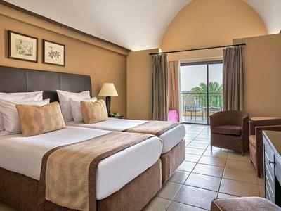 Chambre d'hôtel lumineuse avec deux lits simples, balcon et vue sur la piscine.