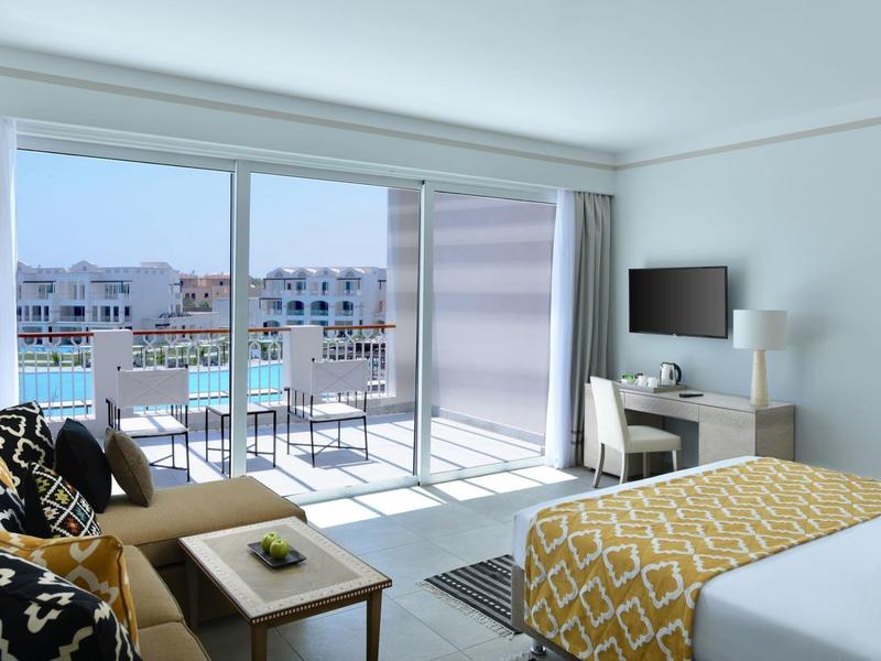 Helles Hotelzimmer mit großem Bett, Terrasse, Meerblick und moderner Einrichtung in neutralen Tönen.