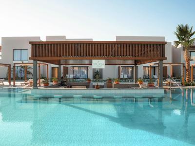 Piscina moderna dell'hotel con lettini e pergolati davanti a un edificio di due piani sotto un cielo limpido.