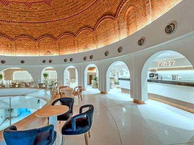 Ampio interno luminoso con archi e sedute sotto una cupola decorata.