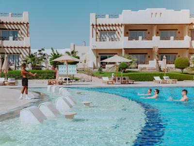 Hotel pool with people, lounge chairs, and umbrellas in front of a multi-story hotel building.
