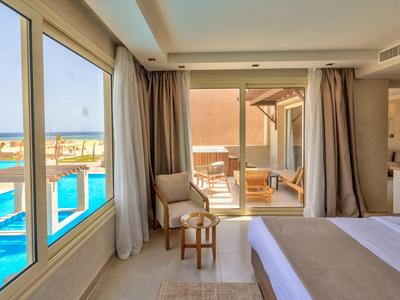 Helles Schlafzimmer mit großen Fenstern, Blick auf Pool, helle Vorhänge, Holzmöbel und Terrasse.