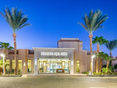 Hotelentree bij schemering met palmbomen en verlichte borden tegen een heldere lucht.