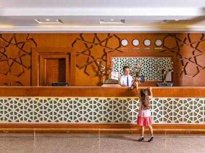 Hotel lobby met houten receptiebalie, geometrische wanddecoraties en gast bij balie.