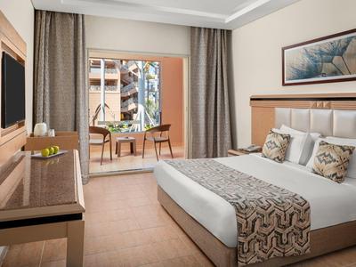 Hotelkamer met een groot bed, sierkussens, bureau en balkon met zitje en uitzicht.