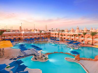 Grande piscine d'hôtel avec chaises longues bleues et palmiers au coucher du soleil
