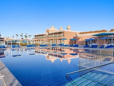 Grand bassin d'hôtel avec eau bleue, parasols et bâtiment à plusieurs étages en arrière-plan.