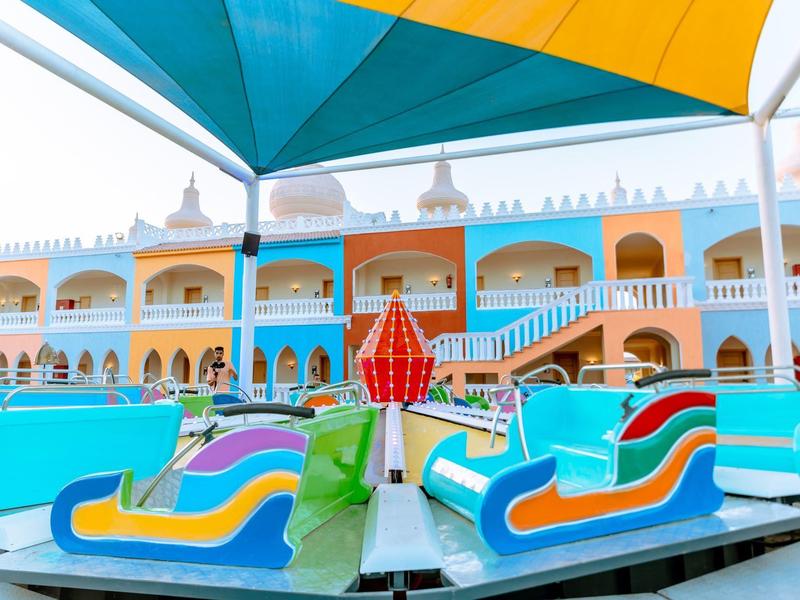 Giostra colorata con sedili davanti a un hotel architettonico vivace sotto un cielo limpido.