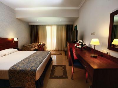 Chambre d'hôtel confortable avec grand lit double, bureau et fauteuil près de la fenêtre.