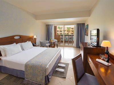 Chambre d'hôtel spacieuse avec lit double, bureau, TV et balcon avec chaises.