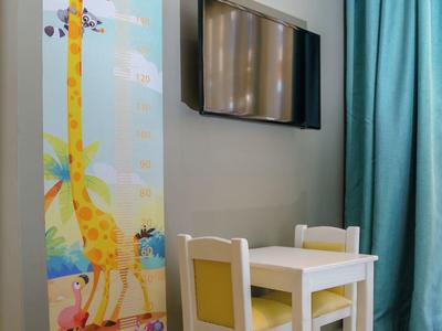 Area giochi per bambini con metro giraffa, piccolo tavolo e due sedie vicino a una tenda blu.