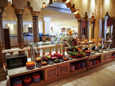 Buffet allestito in un ristorante con illuminazione calda, colonne in legno ed elementi decorativi.