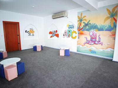 Ampia stanza con moquette grigia, cuscini colorati e murales tropicali.