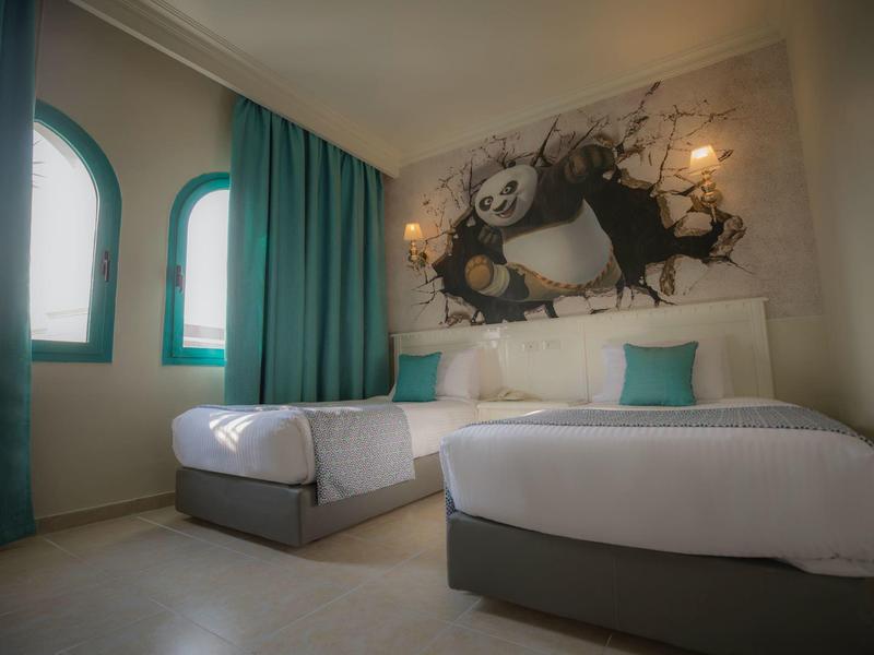 Camera d'hotel con due letti, tende turchesi e un grande murale con un panda.