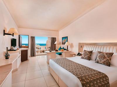 Ampia camera d'hotel con letto king, vista oceano e balcone con posti a sedere.