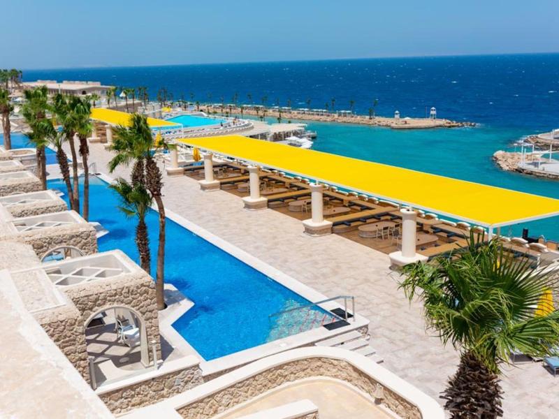Piscina luminosa con tende gialle e palme vicino al mare turchese in una giornata soleggiata.