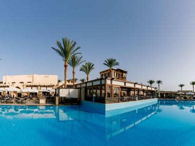 Großer Outdoor-Pool mit Palmen vor einem modernen Hotel bei klarem Himmel.