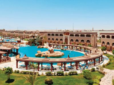 Gran piscina al aire libre con sombrillas y tumbonas frente a un hotel de varios pisos bajo un cielo despejado