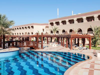 Hotel lujoso con gran piscina, palmeras y áreas cubiertas bajo un cielo azul.